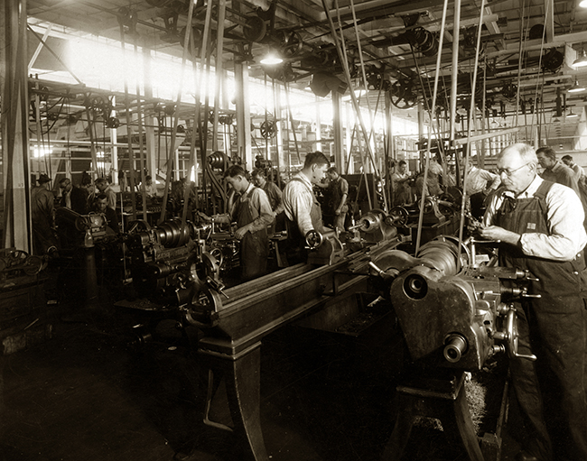 An old black and white photo of an old factory and its workers.